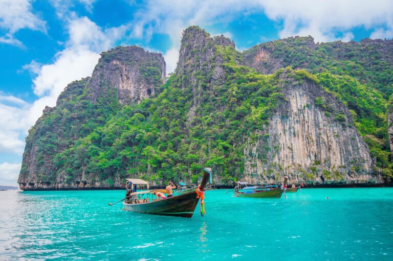 Longtail boats in the turquoise water of Maya Bay, Phi Phi Island, Krabi, Thailand, below green limestone cliffs.