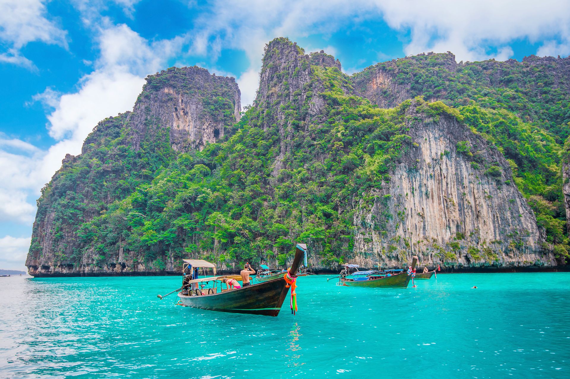 Longtail boats in the turquoise water of Maya Bay, Phi Phi Island, Krabi, Thailand, below green limestone cliffs.
